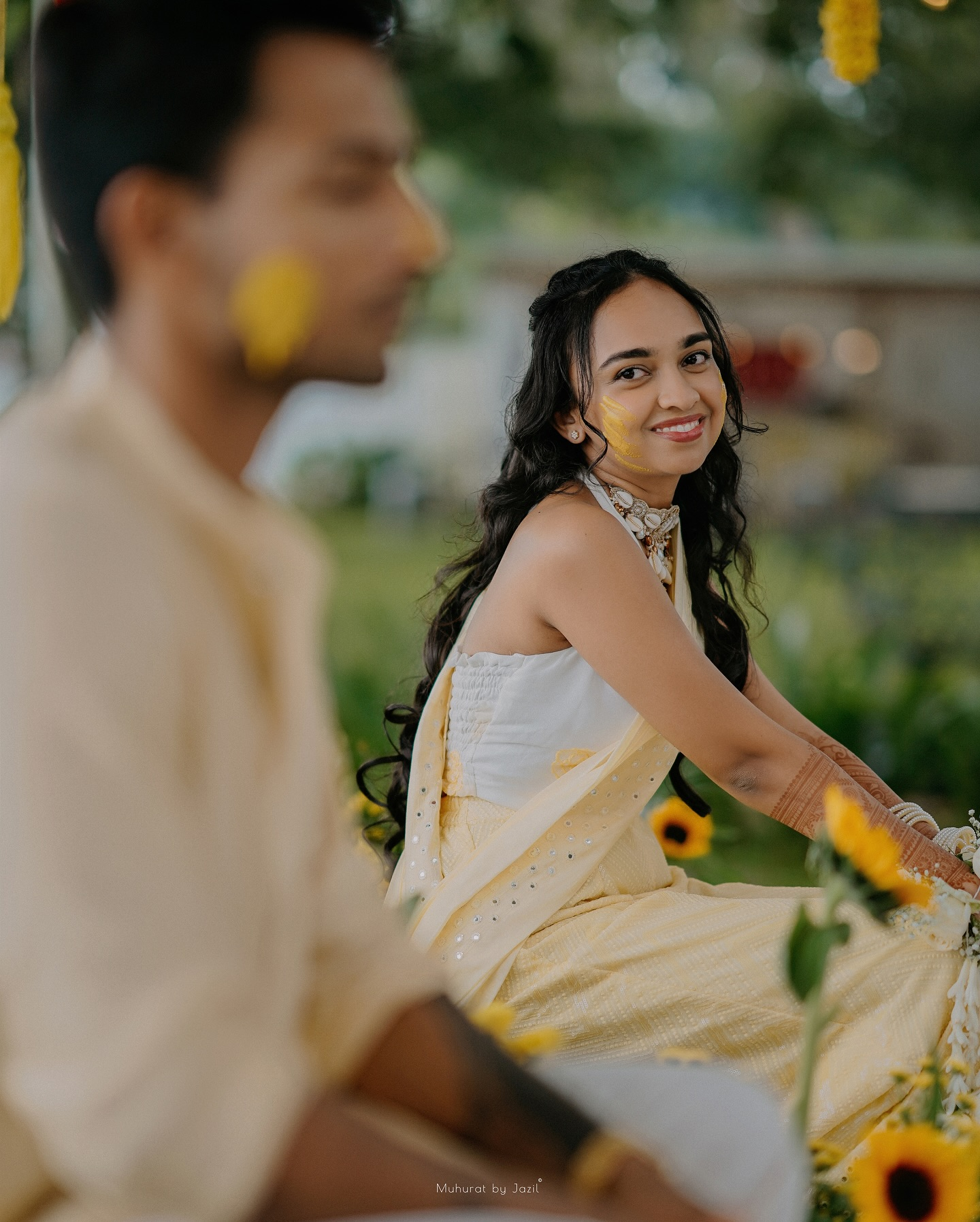A bride smiling across at her partner during a haldi celebration