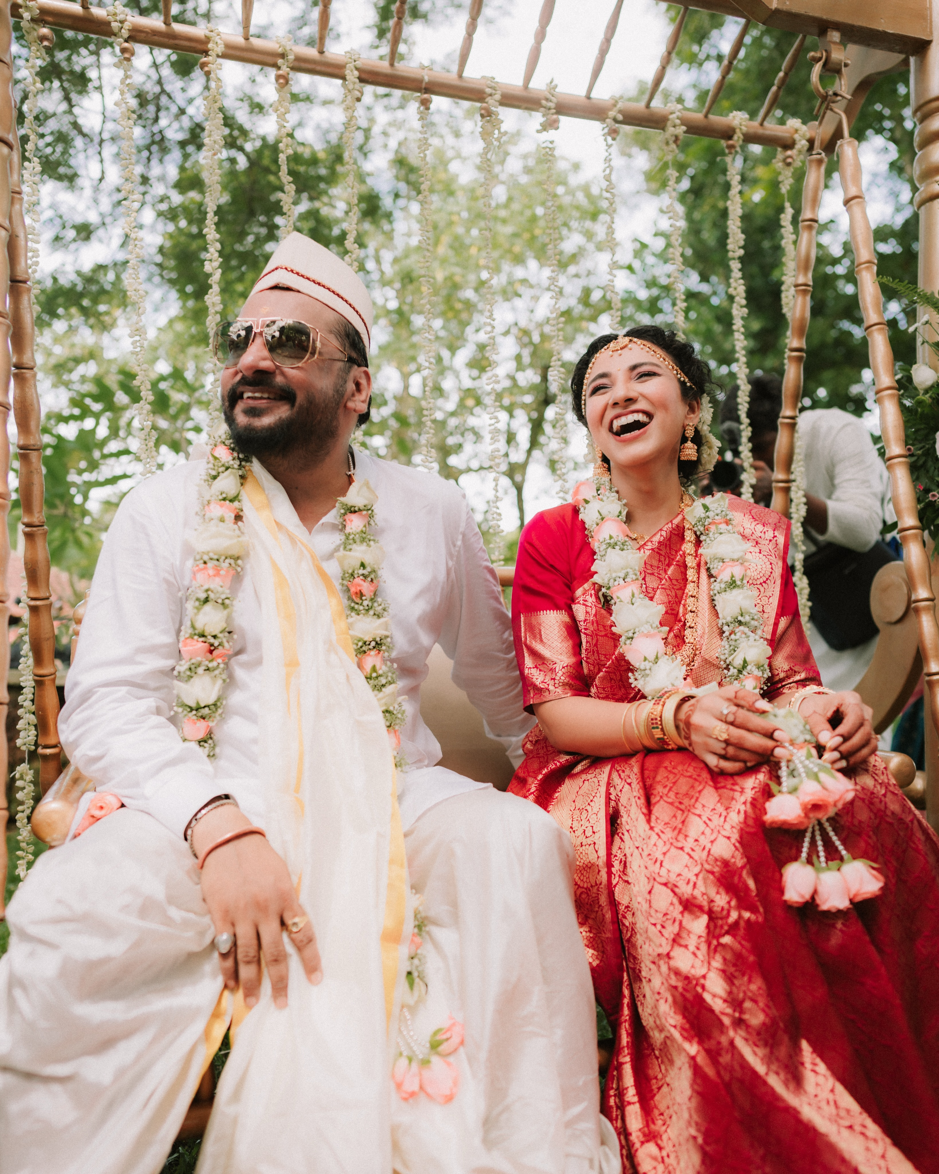 A newlywed couple laughing together beneath a flower-draped canopy